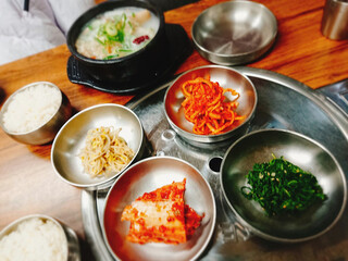 Delicious Korean food includes vegetable pancakes, kimchi, roast pork, a chicken soup, bibimbap, cold side dishes, ox knee soup and rice