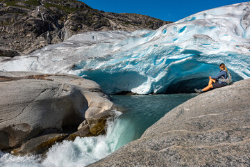 Norway Travel, Young Woman with a backpack admires Nigardsbreen Nigar Glacier arm of Jostedalsbreen located in Gaupne Jostedalen valley Norway
