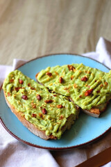 Turquoise plate with two pieces of avocado toast on wooden table. Selective focus.