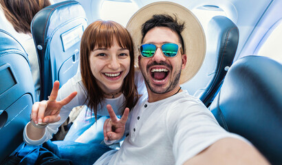 Happy tourist taking selfie inside airplane - Cheerful couple on summer vacation - Passengers...