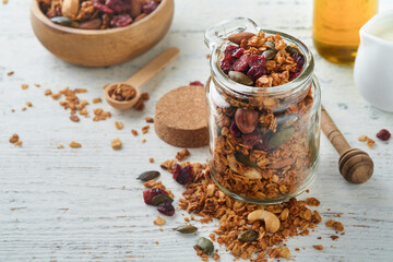 Homemade granola in glass jar with greek yogurt or milk and cashews, almonds, pumpkin with dried cranberry seeds in on white rustic wooden table background. Healthy energy breakfast or snack. Top view