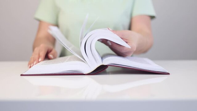 The girl is looking through a book on a white table.