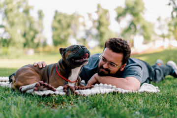 bearded man resting in the park with his pet dog french bulldog outdoors lying on a sheet summer...