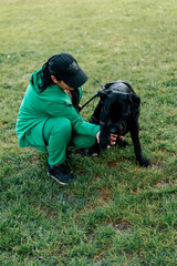 a woman trains a black dog of a large Cane Corso breed on a walk in the park the dog follows the owner's commands