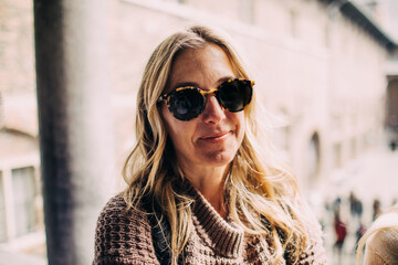 middle age blonde woman wearing sunglasses and a sweater smiles pensively at the camera