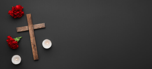 Wooden cross, carnation flowers and candles on dark background with space for text. Funeral concept