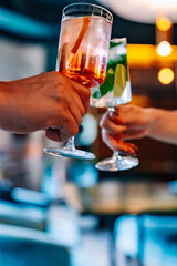 hands of man and women holding and clinking glasses cocktails in restaurant