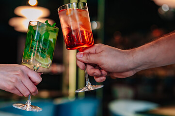 hands of man and women holding and clinking glasses cocktails in restaurant