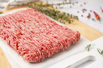 Board with fresh minced meat, thyme and peppercorns on white grunge background