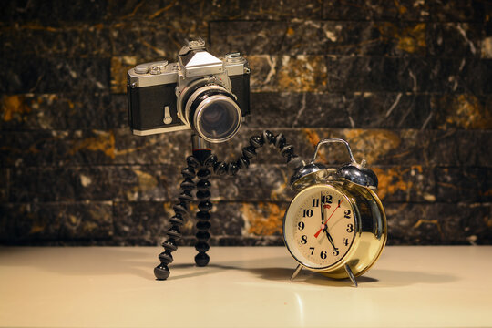 A photo of an old analog camera turning off a mechanical alarm clock 