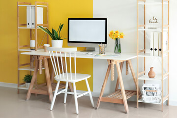 Stylish interior of office with modern PC and beautiful narcissus flowers