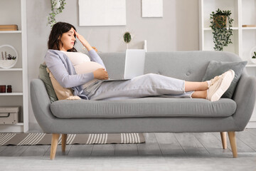 Fototapeta premium Tired young pregnant woman working with laptop on sofa at home