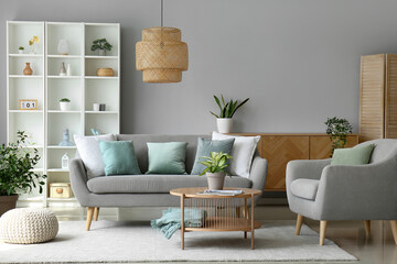 Interior of stylish living room with grey sofa, armchair and houseplant on coffee table