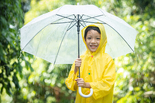 Portrait Asian kid holding an umbrella with raindrops. Happy Asian little child boy having fun playing with the rain in the evening sunlight.