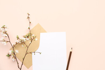 Blooming tree branch with white flowers, blank paper sheet, pencil and envelope on beige background