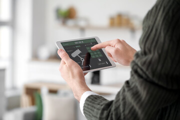 Young man using smart home security system control panel in kitchen, closeup
