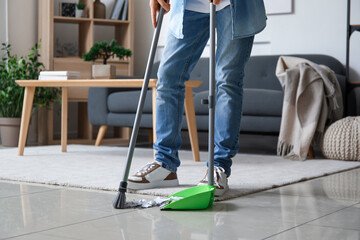 Young man sweeping floor with broom at home