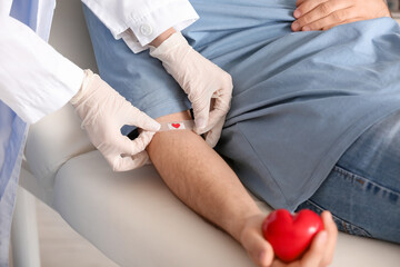 Female doctor applying medical patch on young donor's arm in clinic, closeup