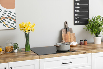 Vase with blooming narcissus flowers on wooden counter in interior of modern kitchen