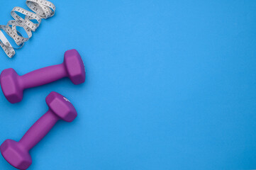 The layout of two rubberized dumbbells of 2 kg in purple,a measuring tape on a blue background,top...