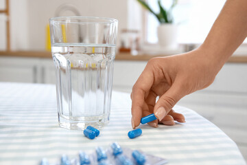 Young pregnant woman taking Folic Acid pill in kitchen, closeup