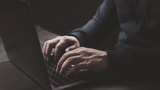 Hacker hand typing on laptop computer keyboard when trying to launch cyber attack to victim security protection. Hacking, Identity theft, phishing, virus and cyber threat concept.