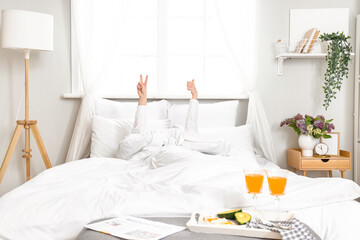 Morning of young woman showing victory gesture and thumb-up in bed