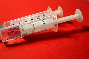 Close-up of two syringes on a red background.