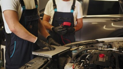 Car mechanic at work. Car an electrician using computer in auto repair shop. Auto electrician using a computer laptop to diagnosing and checking up on car engines parts for fixing and repair.