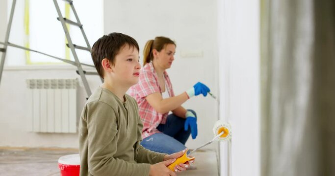 Mother and her son painting wall with paint roller and brush at home