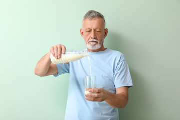 Mature man pouring milk into glass on green background