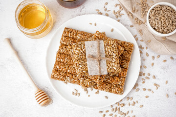Plate with tasty kozinaki, sunflower seeds and jars of honey on white background