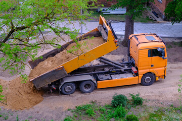 A large orange dump truck unloads the sand.