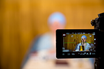 A Jewish woman in a kisui rosh headdress, a teacher of tradition, teaches a lesson. A blurry image is captured by a camera for live broadcast.