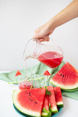 Close-up of fresh watermelon juice or smoothie in glasses with watermelon slices on a white table. A refreshing summer drink is poured into glasses.