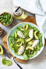 Healthy food, summer healthy eating. Organic green avocado and spinach salad with eggs, green beans, nuts on a stone table. View from above.