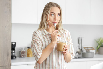Young woman eating tasty nut butter in kitchen