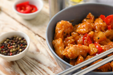 Tasty sweet and sour chicken in bowl with spices on light wooden background, closeup