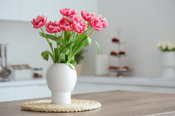 Vase with tulips on table in light kitchen