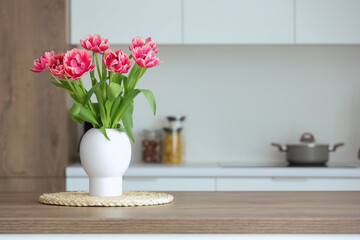 Vase with tulips on table in light kitchen