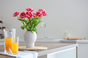 Vase with tulips on table in light kitchen
