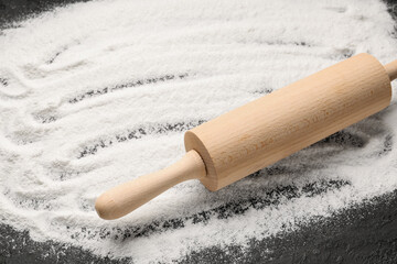 Wooden rolling pin with wheat flour on grunge black background