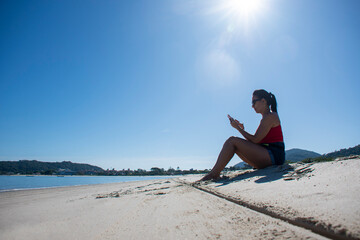 Fototapeta na wymiar Latin woman sitting on the beach sand talking on cell phone
