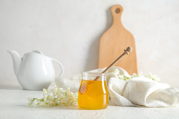Jar of honey with flowers of acacia and teapot on light background