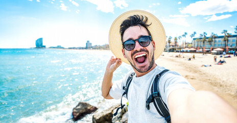 Handsome young man taking selfie with smart mobile phone device outside - Cheerful tourist enjoying summertime at the beach - Life style, traveling and technology concept - obrazy, fototapety, plakaty