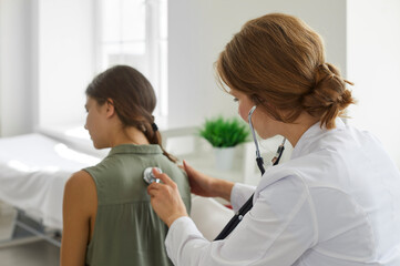 Girl in the clinic for a medical checkup. Female doctor with stethoscope examining child's lungs,...