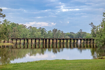 A railroad track bridge over a public lake called Cherokee Lake, in Thomasville Georgia on a Sunny day with a tranquil and peaceful scene - obrazy, fototapety, plakaty