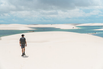 Man in the sand dunes next to a lagoon with white sand at Lencois maranhenses national park in...