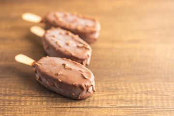 Popsicle, ice cream covered with chocolate on wooden table.