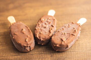 Popsicle, ice cream covered with chocolate on wooden table.